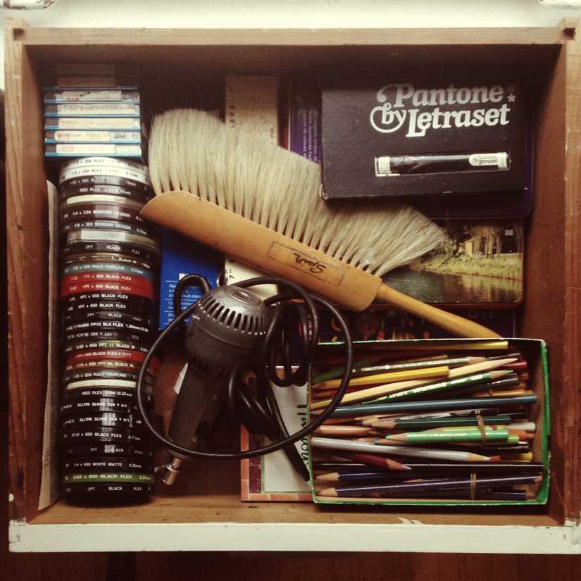Drawer full of calligraphy and art supplies including pencil crayons, electric eraser, brush, and border tape