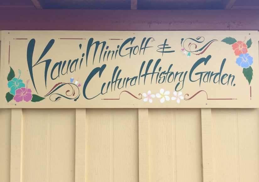 Sign mounted to the side of a shed reading "Kauai Mini Golf & Cultural History Garden"