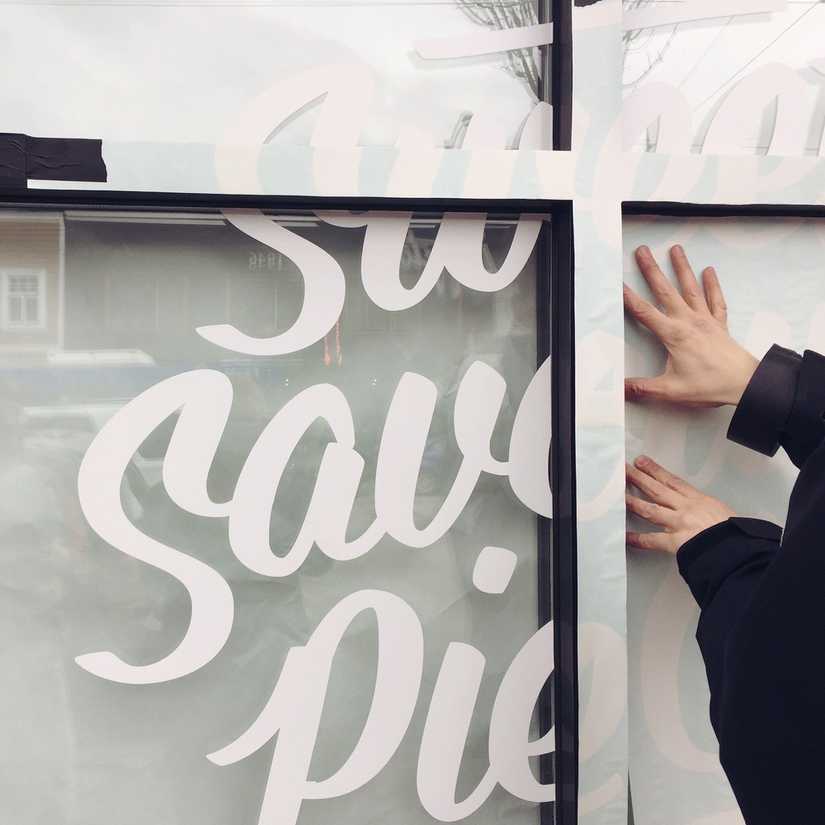 Close up of shop window as the vinyl letters are being applied by a man.